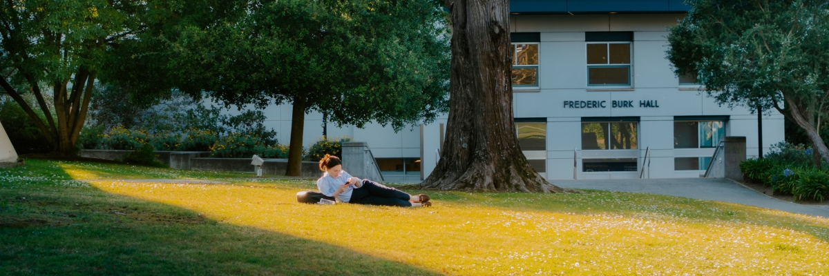 A student lounging on the grass outside of Burk Hall